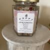 Jar of flower bath salts with a gold lid on a white pedestal