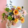 Mixed bouquet in a pink vase with orange, pink, blue, and white flowers