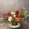 Large mixed floral arrangement in a dark vase with cream, red, and orange blooms