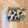 Blue and white floral arrangement in a wooden cart with a doll and lace umbrellas