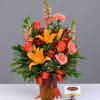 Mixed bouquet in an amber glass vase with orange lilies, roses, and pink carnations