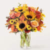 Bouquet of sunflowers, roses, and mums in a clear glass vase