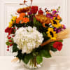 Mixed bouquet with white hydrangea, red roses, sunflowers, and orange blooms in a glass vase