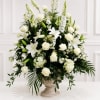White floral arrangement with roses and lilies in a stone pedestal vase