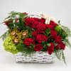 Red roses and orchids arranged in a white basket with a ribbon