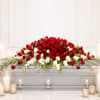Red and white floral casket spray with candles around it