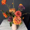 Orange and pink flowers arranged in a pale vase