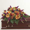 Colorful floral spray on a wooden casket with roses and lilies
