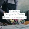 Florist in an apron arranging a pastel pink and white rose bouquet on a wooden table