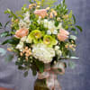 Peach roses, white hydrangea, and green orchids in a glass vase with ribbon