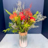 Bright mixed bouquet in a tall metallic vase with red and orange blooms