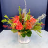 Coral roses and orange pincushion blooms in a clear vase