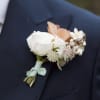 Boutonniere with white and peach flowers pinned to a dark suit jacket