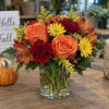 Orange roses and fall flowers arranged in a clear glass vase