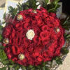Round bouquet of red roses with one white rose and green foliage