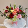 Mixed bouquet of roses, tulips, dahlias, and carnations in a pink vase