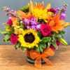 Bright mixed bouquet in a glass vase with sunflowers, roses, lilies, and purple blooms