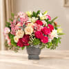 Mixed bouquet of pink roses, lilies, and orchids in a gray vase