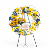 Circular standing wreath of white, yellow, and blue flowers on a black easel