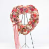 Heart-shaped floral wreath on a stand with pink ribbon