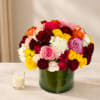 Mixed bouquet of roses in a green glass vase beside a small candle