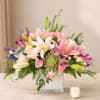 Pink and white lily bouquet in a square glass vase with a candle nearby