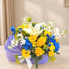 Yellow and blue mixed flower arrangement in a purple box with a white ribbon