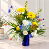 Mixed bouquet in a blue vase with yellow, white, blue, and pink flowers