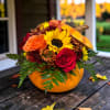 Fall floral arrangement in a pumpkin-shaped container with roses and a sunflower