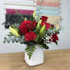 Red roses and carnations in a white vase with lilies and eucalyptus