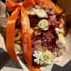 Bouquet of orange, burgundy, and cream flowers with an orange ribbon