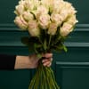 Handheld bouquet of pale pink roses against a dark green background