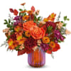 Orange roses and mixed fall flowers in a striped glass vase