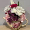 Mixed bouquet of white, pink, and purple flowers in a cream teapot vase