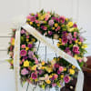 Large floral wreath with pink, yellow, and purple blooms on a stand with white ribbons