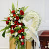 Standing funeral spray with red roses and white flowers beside a casket