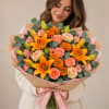 Woman holding a bouquet of orange lilies and pink roses wrapped in paper