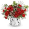 Red roses and carnations in a clear glass vase with pinecones and evergreen accents