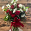 Red roses and white daisies in a glass vase with a red ribbon