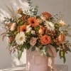 Orange and white mixed flower arrangement in a pink hat box with ribbon