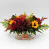 Autumn floral arrangement with sunflowers and red mums in a pumpkin-decorated container.