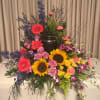 Large floral arrangement with sunflowers, roses, gerberas, and orchids around an urn