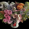 Lush arrangement with pink roses, mini calla lilies, orange mums, blue flowers and ornamental cabbage in a footed vase