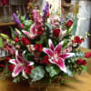Basket arrangement of red roses and pink lilies with purple accents