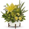 Yellow lilies and green flowers in a white container on wooden legs