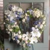 Heart-shaped floral wreath with white lilies, roses, and blue flowers on an easel