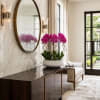 Pink orchid arrangement in a white bowl on a dark console table
