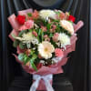 Mixed bouquet of pink and white flowers wrapped in pink paper with a white ribbon