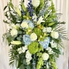 Tall floral spray with white roses, lilies, blue hydrangeas, and green blooms
