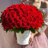 Large round arrangement of red roses in a white hatbox held by a person in a sequin dress